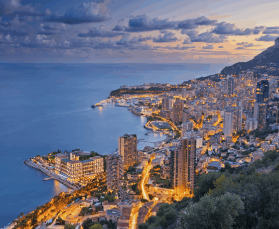 Abendliche Panoramaaufnahme von Monaco mit Blick auf das Meer und die beleuchtete Stadt.